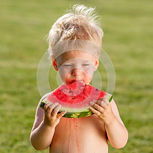 One year old baby boy eating watermelon in the garden