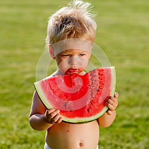 One year old baby boy eating watermelon in the garden