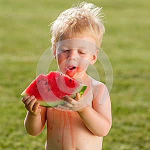 One year old baby boy eating watermelon in the garden