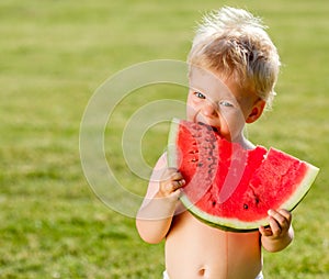 One year old baby boy eating watermelon in the garden