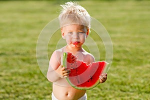 One year old baby boy eating watermelon in the garden