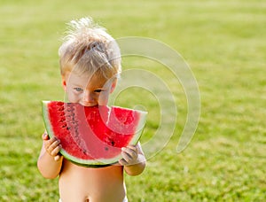 One year old baby boy eating watermelon in the garden