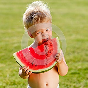 One year old baby boy eating watermelon in the garden