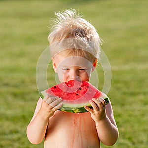 One year old baby boy eating watermelon in the garden