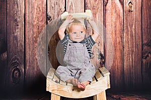 One year old baby boy sitting on chair in front of wooden background. One year concept with copy space