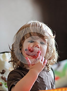 One year old baby girl eating delicious blueberry and black currant pie with her face dirty