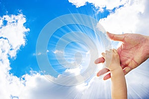 A one year old baby girl is grabbing her parent's hand, with a background of blue sky and white clouds