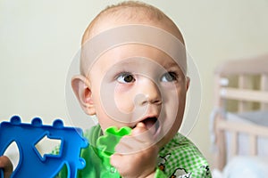 One-year-old baby gnaws a plastic toy because his teething. Little cheerful boy in a light green suit with sheep.