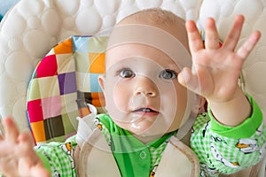 One year old baby looks and raises handles up. Little cheerful boy in a light green suit with sheep.