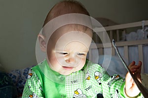 One year old baby is sitting and attentively looking somewhere. Little cheerful boy in a light green suit with sheep.