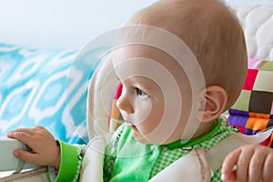 One year old baby is sitting and attentively looking somewhere. Little cheerful boy in a light green suit with sheep.