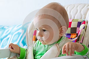 One year old baby is sitting and attentively looking somewhere. Little cheerful boy in a light green suit with sheep.