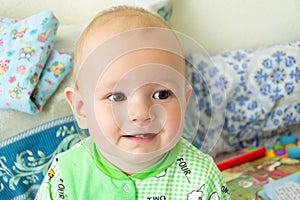 One year old baby is sitting and attentively looking somewhere. Little cheerful boy in a light green suit with sheep.