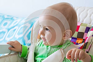 One year old baby is sitting and attentively looking somewhere. Little cheerful boy in a light green suit with sheep.