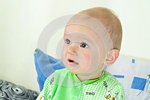 One year old baby is sitting and attentively looking somewhere. Little cheerful boy in a light green suit with sheep.