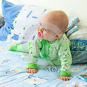 One year old baby vigorously crawls to his goal. Little cheerful boy in a light green suit with sheep.