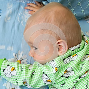 One year old baby vigorously crawls to his goal. Little cheerful boy in a light green suit with sheep.