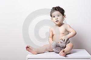 One year old baby wearing a diaper and playing with a doll on a white table