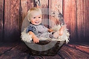 One year old blond baby boy sitting in basket and smiling  in front of wooden background in studio. Child studio photoshot with