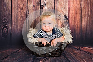 One year old blond baby boy sitting in basket and smiling  in front of wooden background in studio. Child studio photoshot with