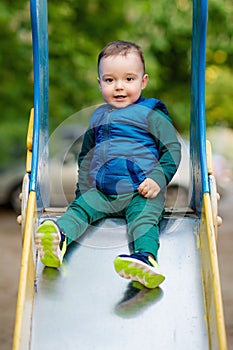 One-year-old boy plays on a playground next to a slide.