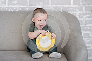 The one-year-old boy is sitting on a gray sofa with a book
