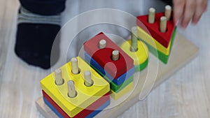 A one year old child puts geometric shapes on pin in wooden construction. Close-up of kid's hand and toy