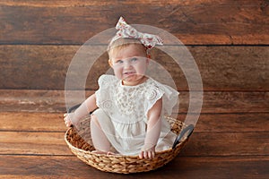 One year old girl. With headband. Girl sitting in a wicker basket.