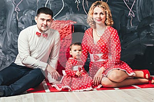 . A one-year-old girl on her birthday in a red dress in a white circle with her parents sits near a big figure alone