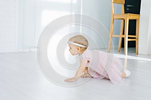 A one-year-old girl in a pink dress crawls on the floor in the children`s room