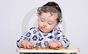 One year old kid eating a slice of birthday smash cake by himself.