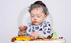 One year old kid eating a slice of birthday smash cake by himself.