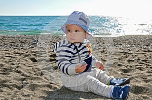 The one-year-old kid in a hat sitting on the beach