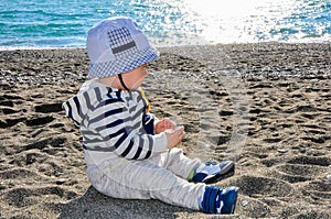 The one-year-old kid in a hat sitting on the beach