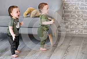 One year old  twin boys are standing near the sofa