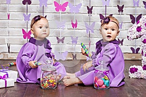 One-year-old twins on the birthday. Cute twin sisters celebrating their 1th birthday. Little twins girl siting on a floor and