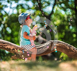 One years old little girl blowing soap bubbles in summer park