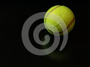 One yellow green tennis ball on dark glossy surface