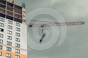 One yellow high-rise crane hauling plate against a house and gray sky during the construction phase