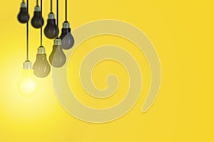 One yellow light bulb of others black light bulb hanging from ceiling with yellow background.