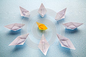 One yellow paper boat is surrounded by many large white boats.