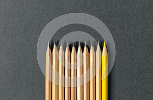 One yellow pencil standing out from the series of gray pencils.