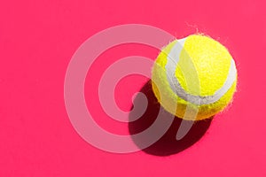 One yellow tennis ball on fuchsia pink background in bright sunlight sports active lifestyle competition victory concentration