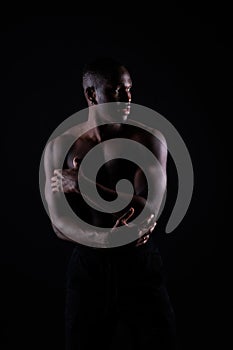 One young african muscular build man standing topless silhouette  on black background