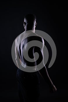 One young african muscular build man standing topless silhouette isolated on black background