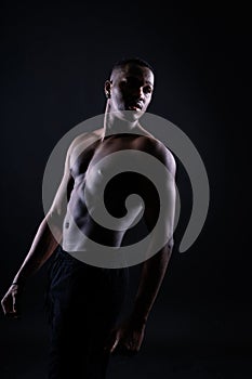 One young african muscular build man standing topless silhouette isolated on black background