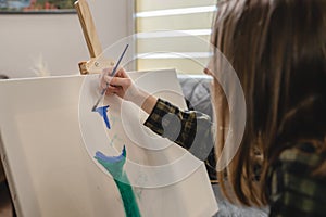 One young beautiful caucasian woman artist sitting on the bed sofa at home painting on the canvas holding paintbrush art and