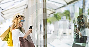 One young beautiful woman shopping and buying clothes alone in the mall carrying shopping bags. Female using phone