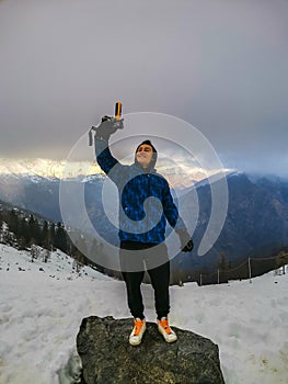 One young boy taking selfie footage with action cam of him standing and smiling with great mountain view in background. Concept of