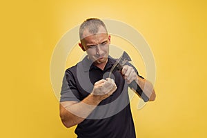 One young brutal man, firefighter cutting nails with an axe over yellow studio background.